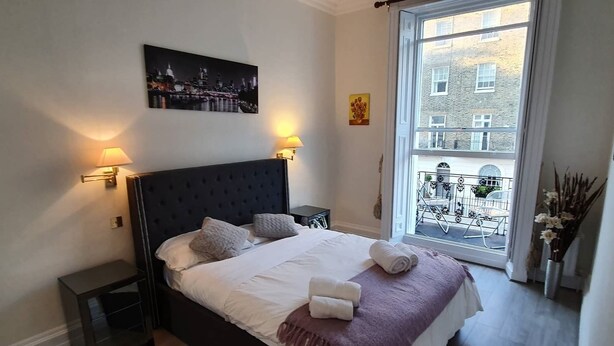 A neatly made bed with pillows and towels, a dark headboard, and two wall-mounted lamps.