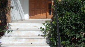 A wooden door with a glass panel, a white exterior wall, and a brick archway. - Red Sun (Chios)