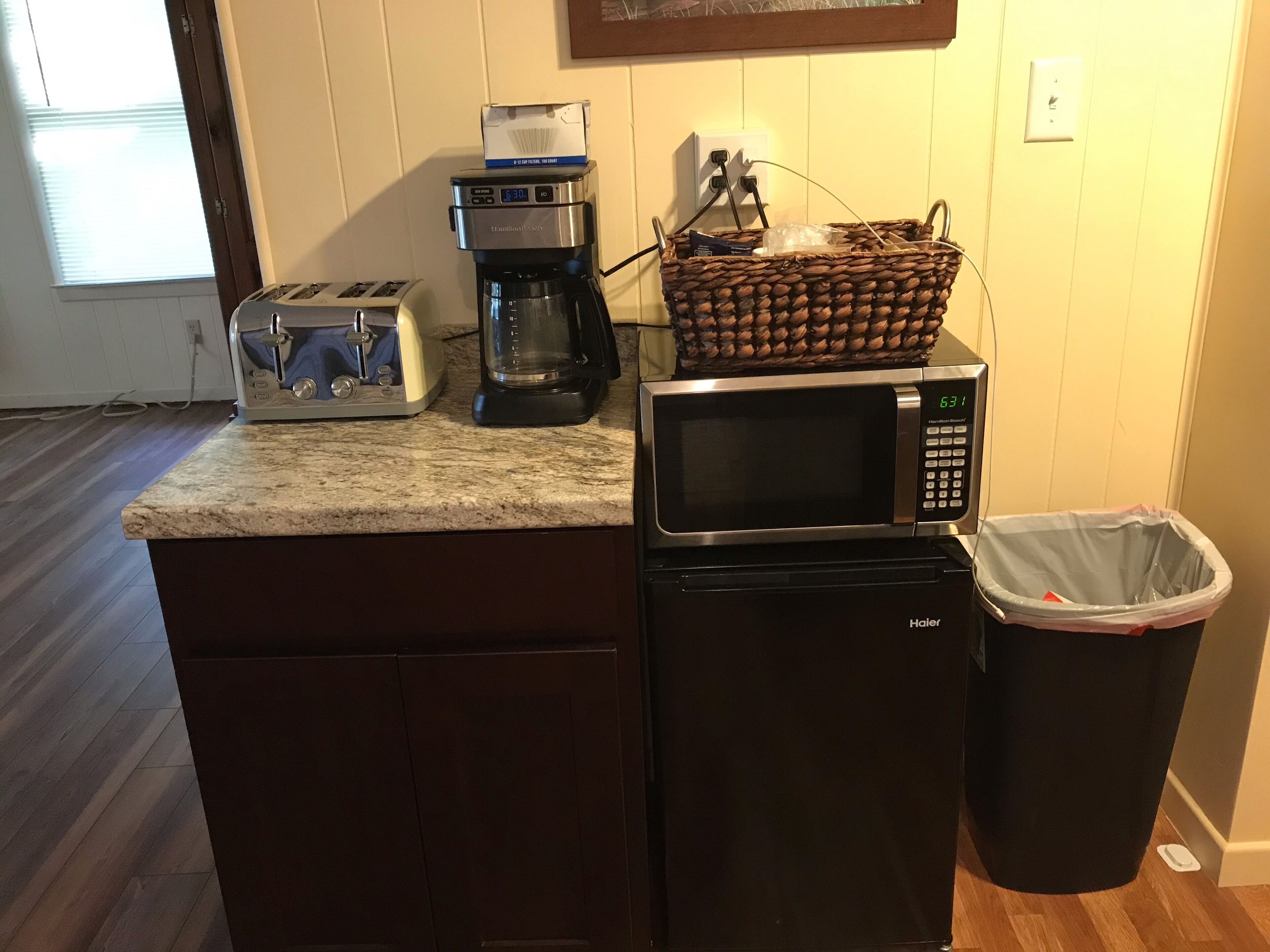 A compact kitchen with a toaster, coffee maker, microwave, and a trash bin.
