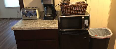 A compact kitchen with a toaster, coffee maker, microwave, and a trash bin.