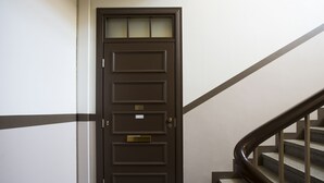 Eine dunkelbraune Tür mit Messingbeschlägen und einer Namensschild, die zu einer Treppe mit Handlauf und Teppichstufen führt.