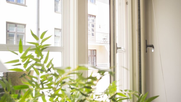 Blick durch ein Fenster mit weißem Rahmen auf ein Gebäude mit zahlreichen Fenstern und Balkonen.