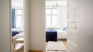 Ein schmaler Flur, der zu einem Schlafzimmer mit Fenster, Heizkörper und einer weißen Tür führt.