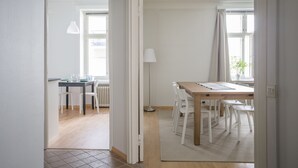 Ein Essbereich mit einem Holztisch, weißen Stühlen, einer Lampe und Blick ins Freie durch ein Fenster.