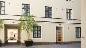 Ein Gebäude mit einer beigefarbenen Fassade, zahlreichen Fenstern und einem zentralen Eingang mit einer Holztür.