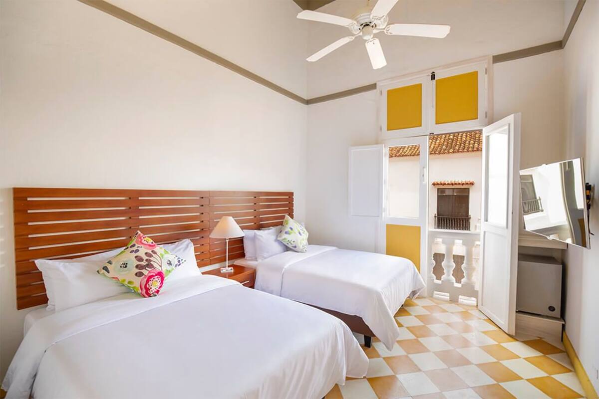 A hotel room with two beds, a ceiling fan, a TV, and a minibar.
