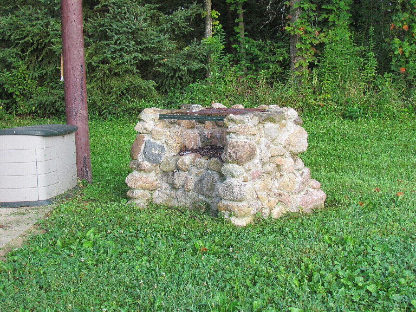 Une construction en pierre surmontée d’un toit métallique, entourée d’herbe et d’arbres.