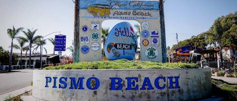 Un cartel de Pismo Beach con varios logotipos e ilustración de un coche antiguo.