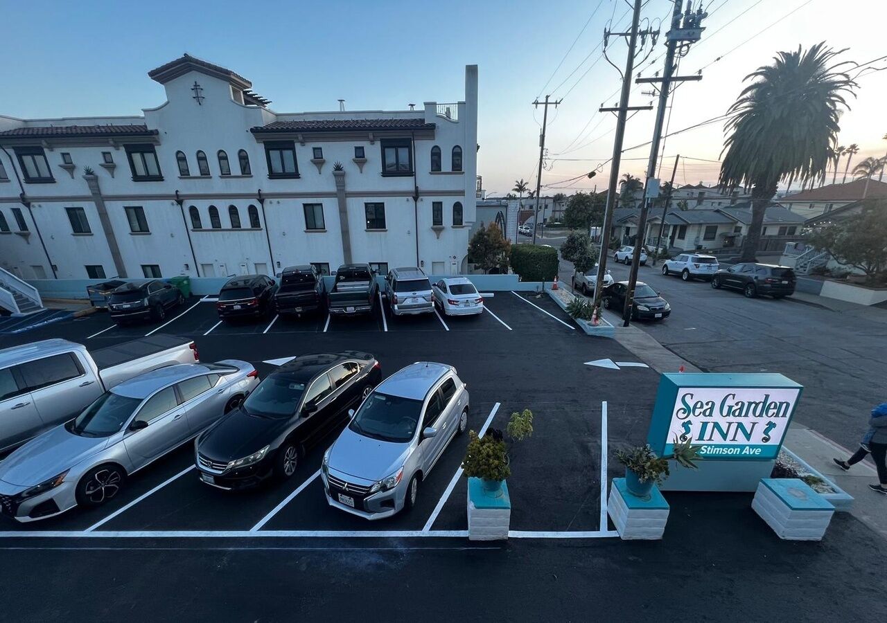 A parking lot with several cars, a building with a sign for 'Sea Garden $Inn,' and a palm tree in the background.