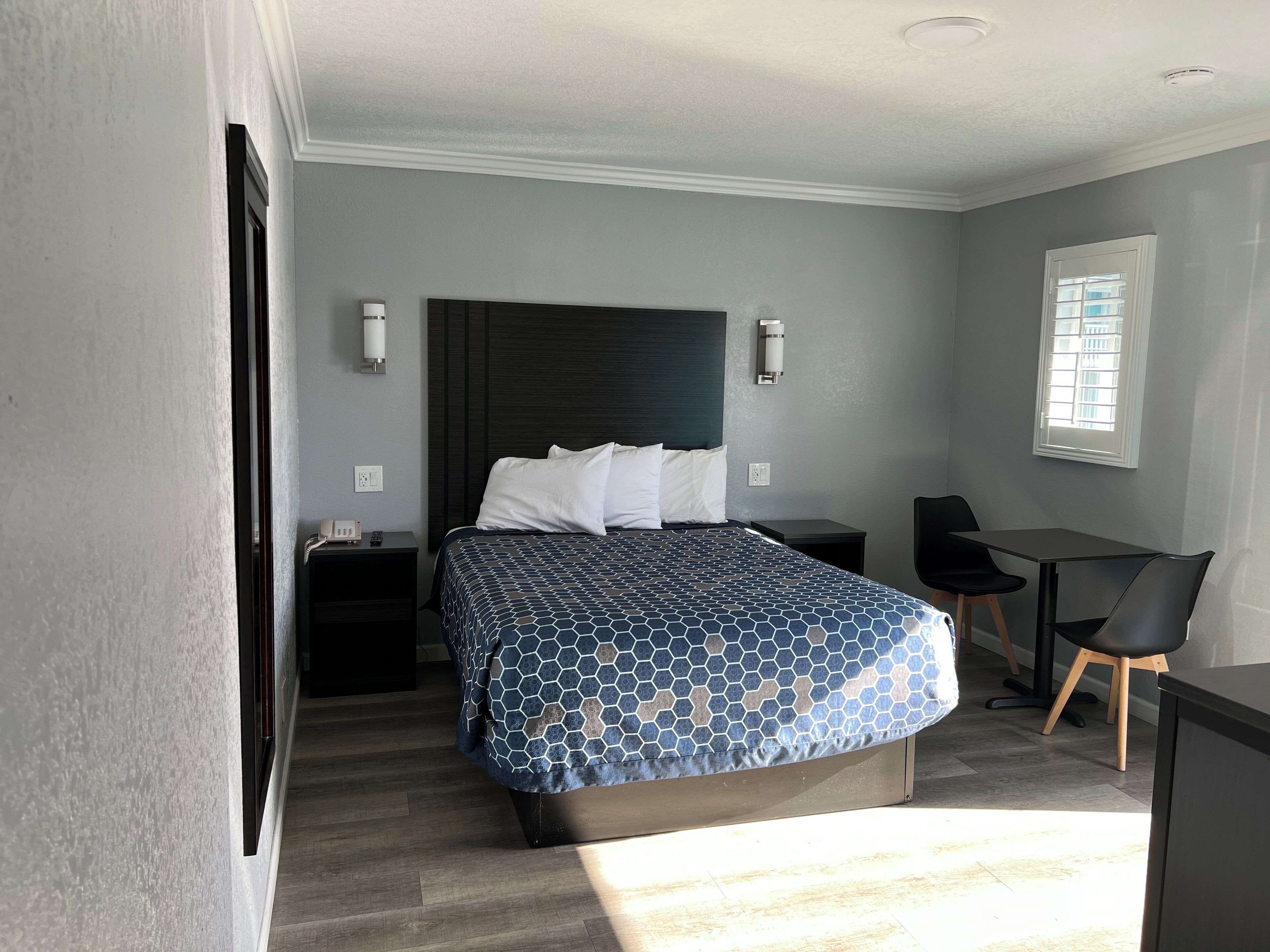 A modern hotel room with a large bed, a desk, a chair, and a window.