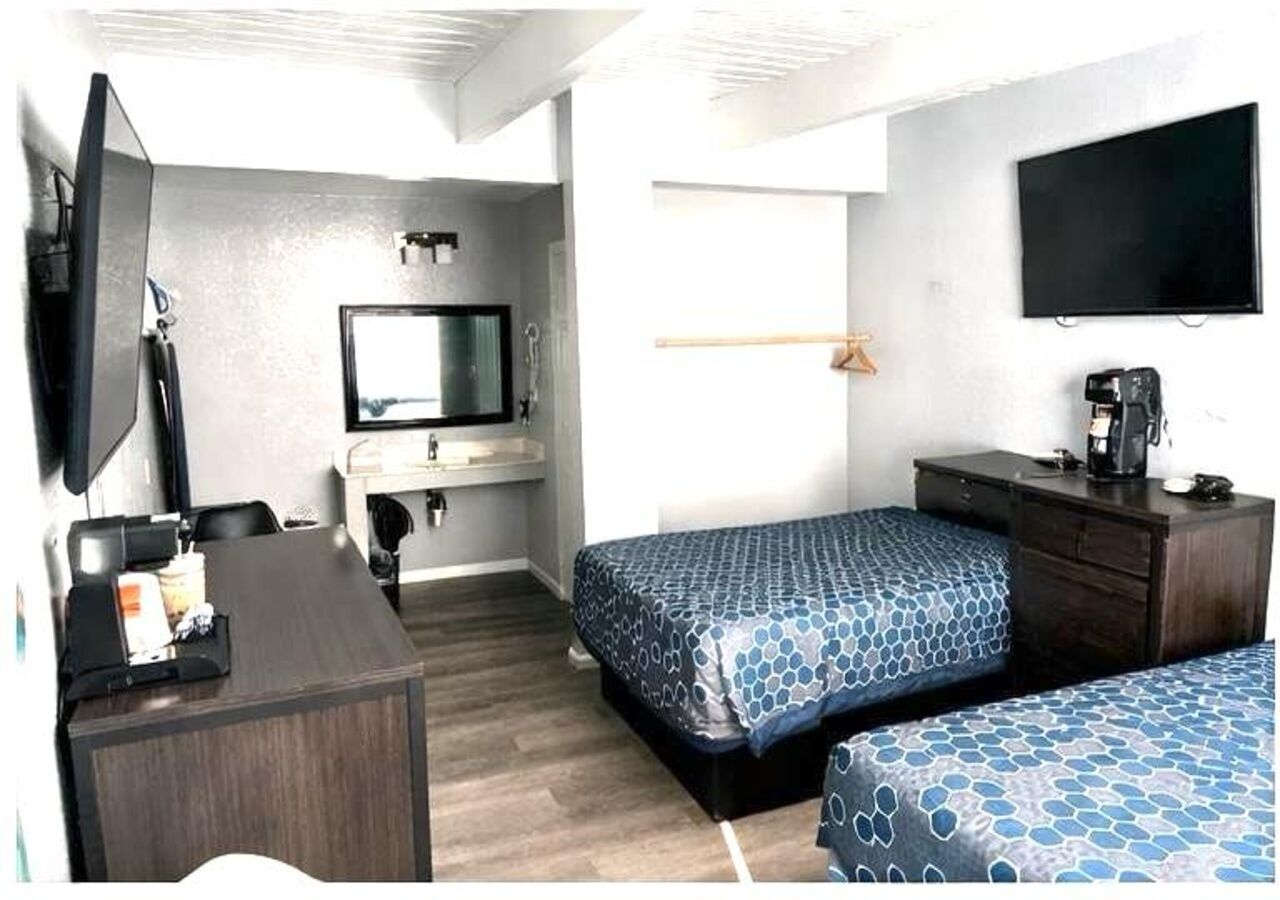 Una habitación con dos camas, un escritorio, un televisor, una cafetera y un espejo.