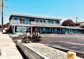 Een tweelaags motel met een balkon op de tweede verdieping, een bord met de tekst 'Sea Garden Inn' en een parkeerplaats ervoor.