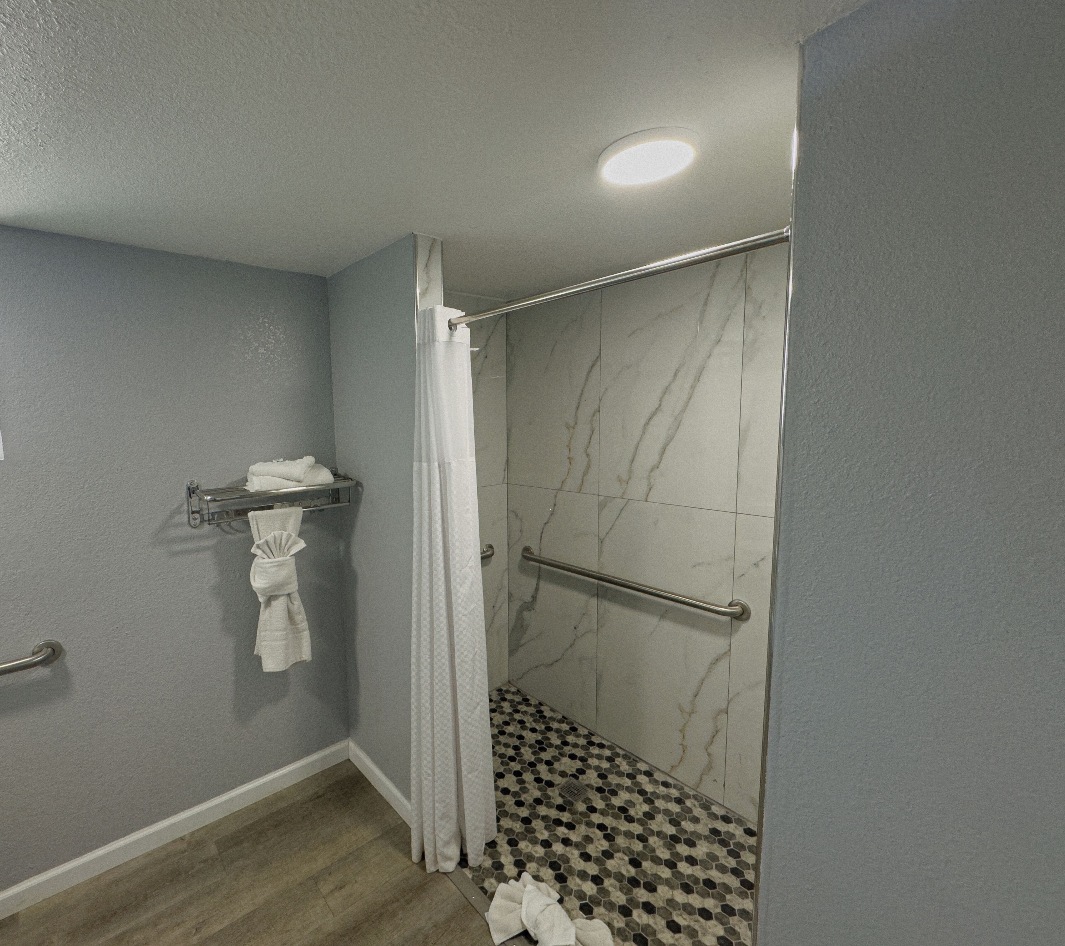 A bathroom with a shower, tiled walls, a towel rack, and a floor with a black and white pattern.