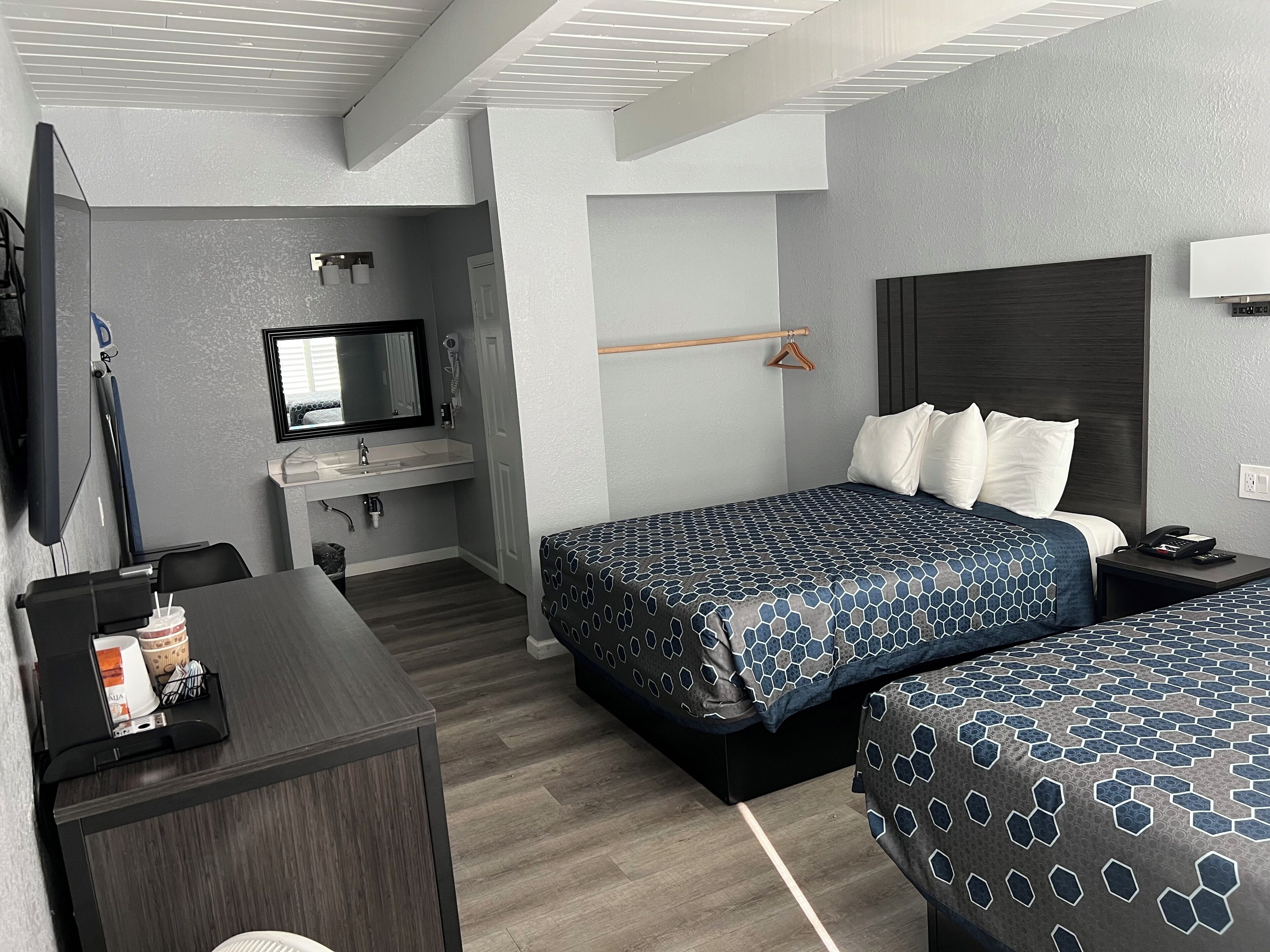 Una habitación de hotel con dos camas, un escritorio, un televisor, un espejo y un baño pequeño.