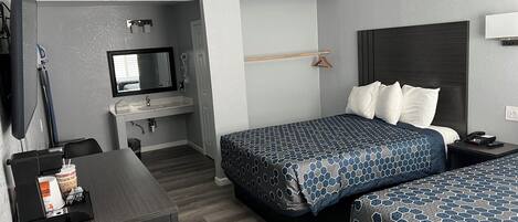 Una habitación de hotel con dos camas, un escritorio, un televisor, un espejo y un baño pequeño.