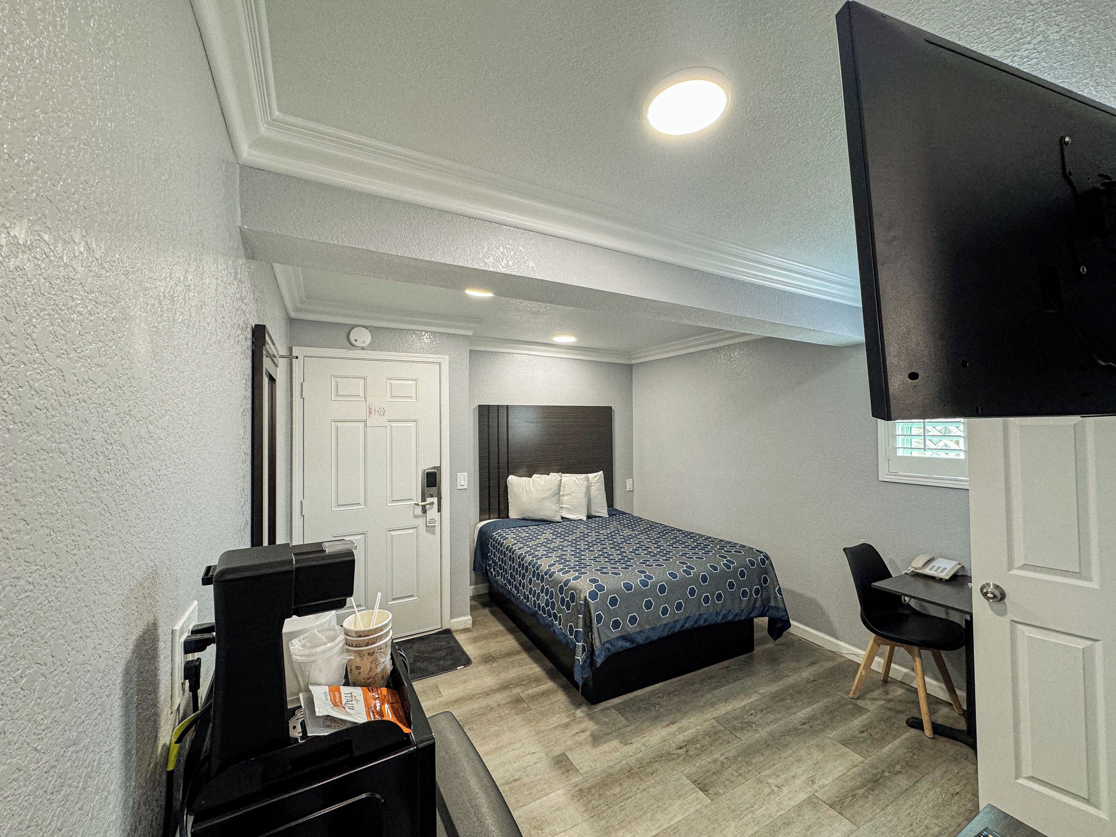 Une chambre d’hôtel avec un lit, un bureau, un téléviseur fixé au mur et une porte avec une fenêtre.