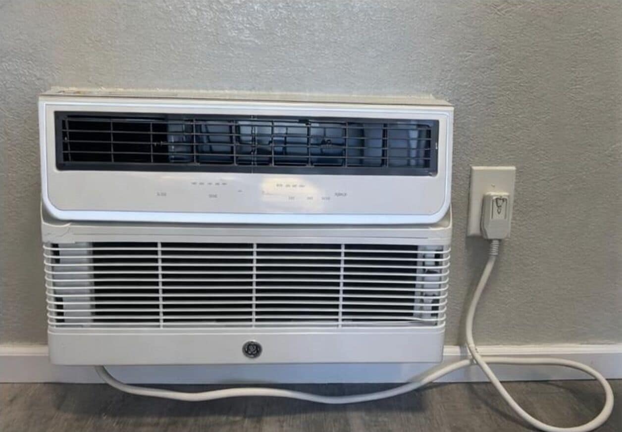 A white portable air conditioner unit with a control panel, connected to a power outlet.