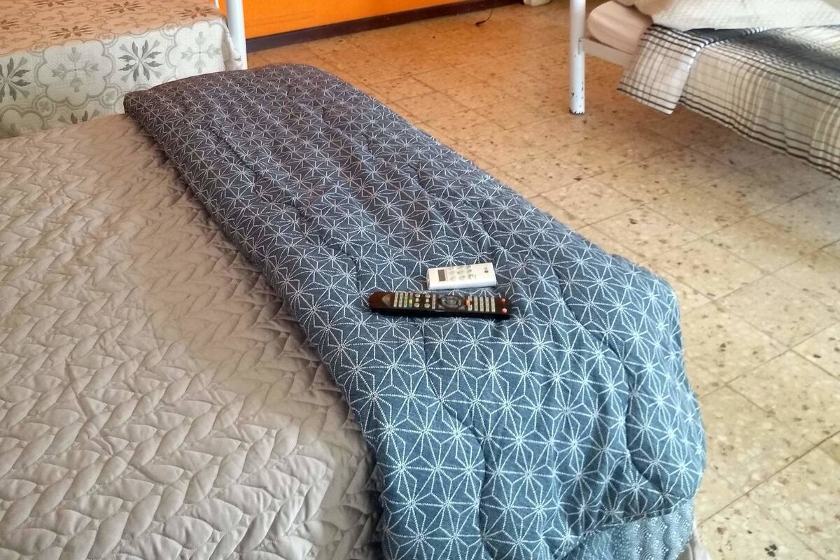 A room with two single beds, a television mounted on the wall, and a door leading to another room.