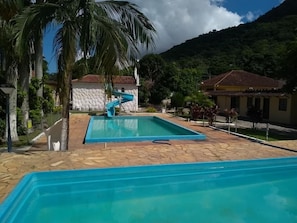 A swimming pool with a slide, surrounded by palm trees and a mountainous backdrop.