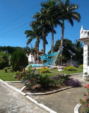 A pool area with a blue slide, palm trees, and a white building with a conical roof.