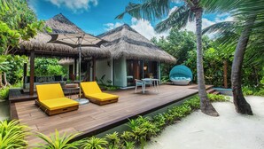 A tropical resort with a wooden deck, yellow lounge chairs, a thatched-roof structure, and a pool area. - Pullman Maldives Resort (Maamutaa Island)