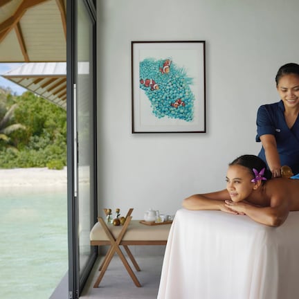 A massage therapy session in a room with a view of a beach and palm trees.
