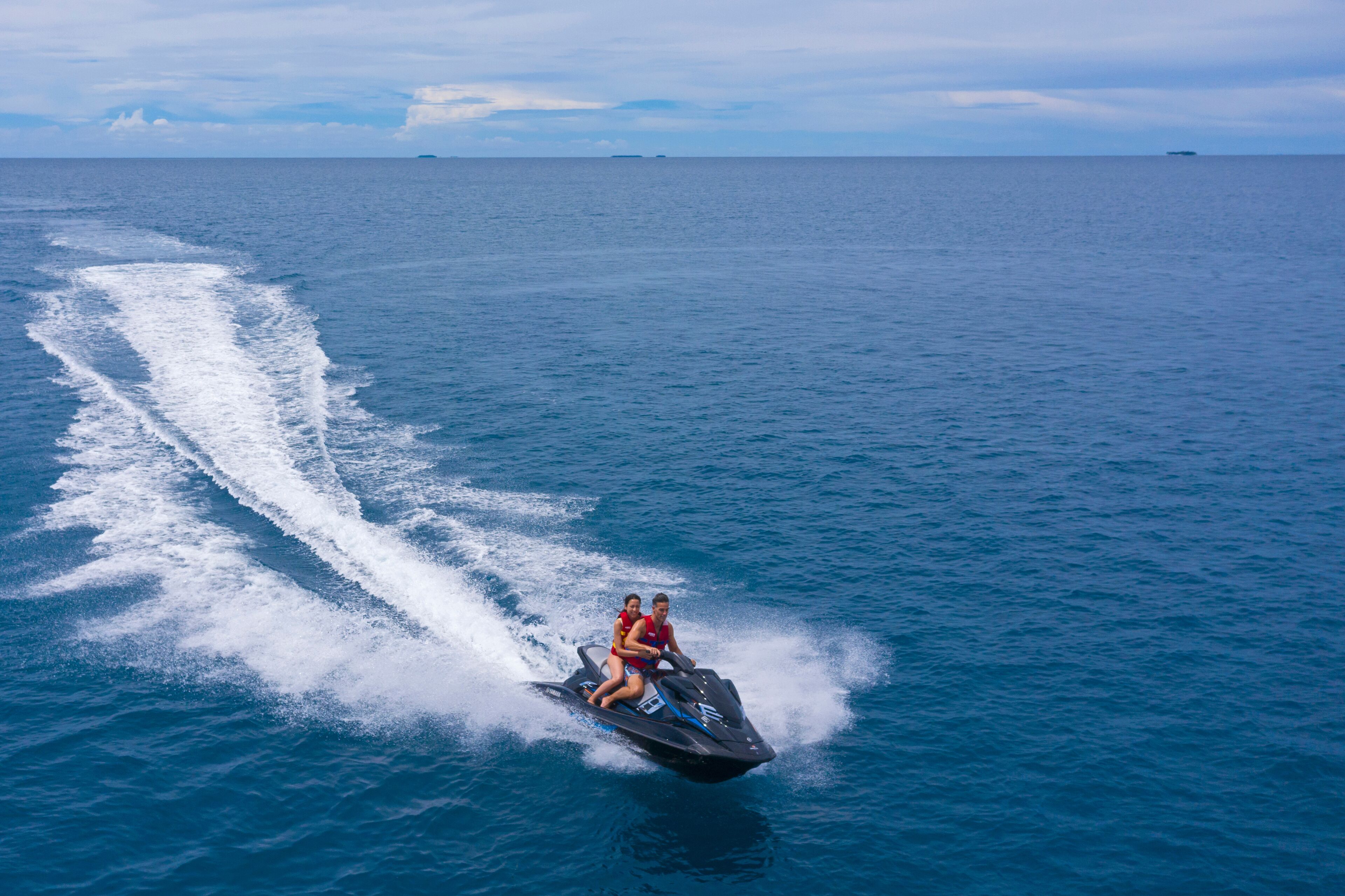 A jet ski with two people on it, moving through a large body of water.