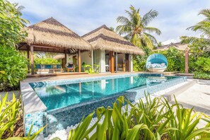 A poolside area with a clear pool, thatched-roof structures, and lush greenery. - Pullman Maldives Resort (Maamutaa Island)