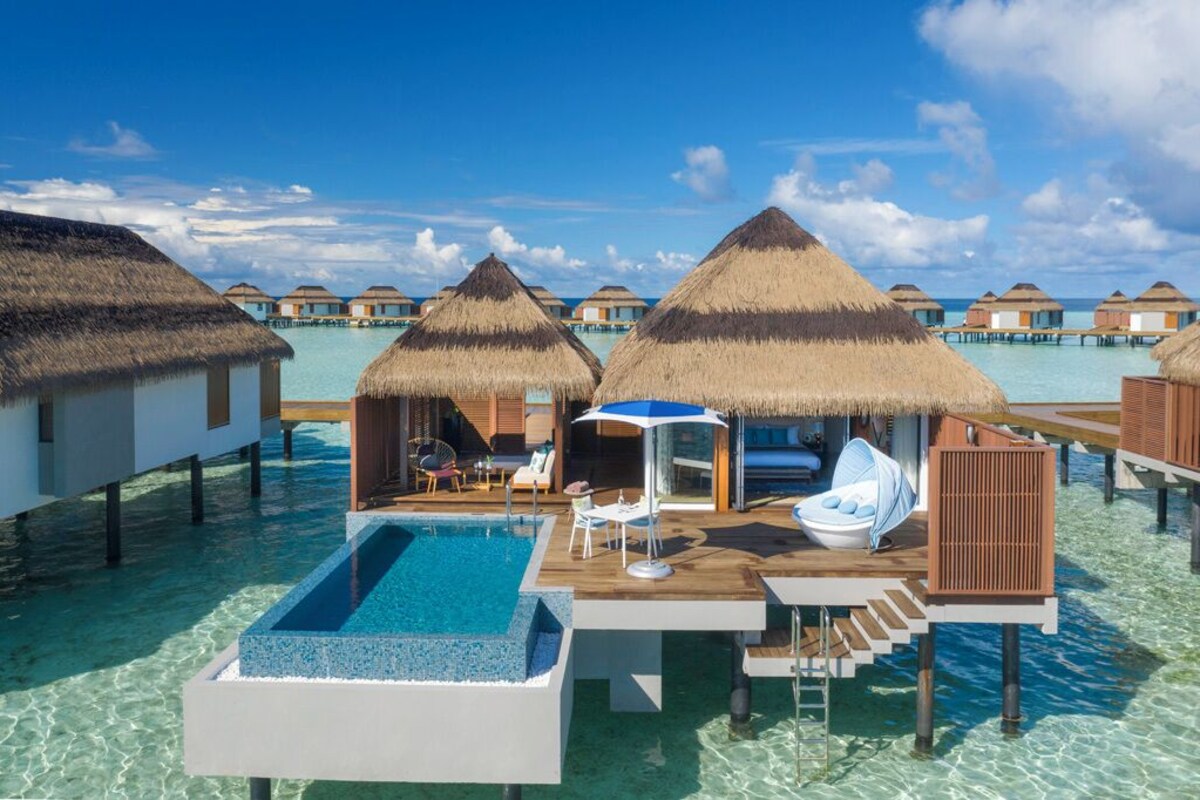 Cabañas sobre el agua con techos de paja, piscina y sillas de descanso.