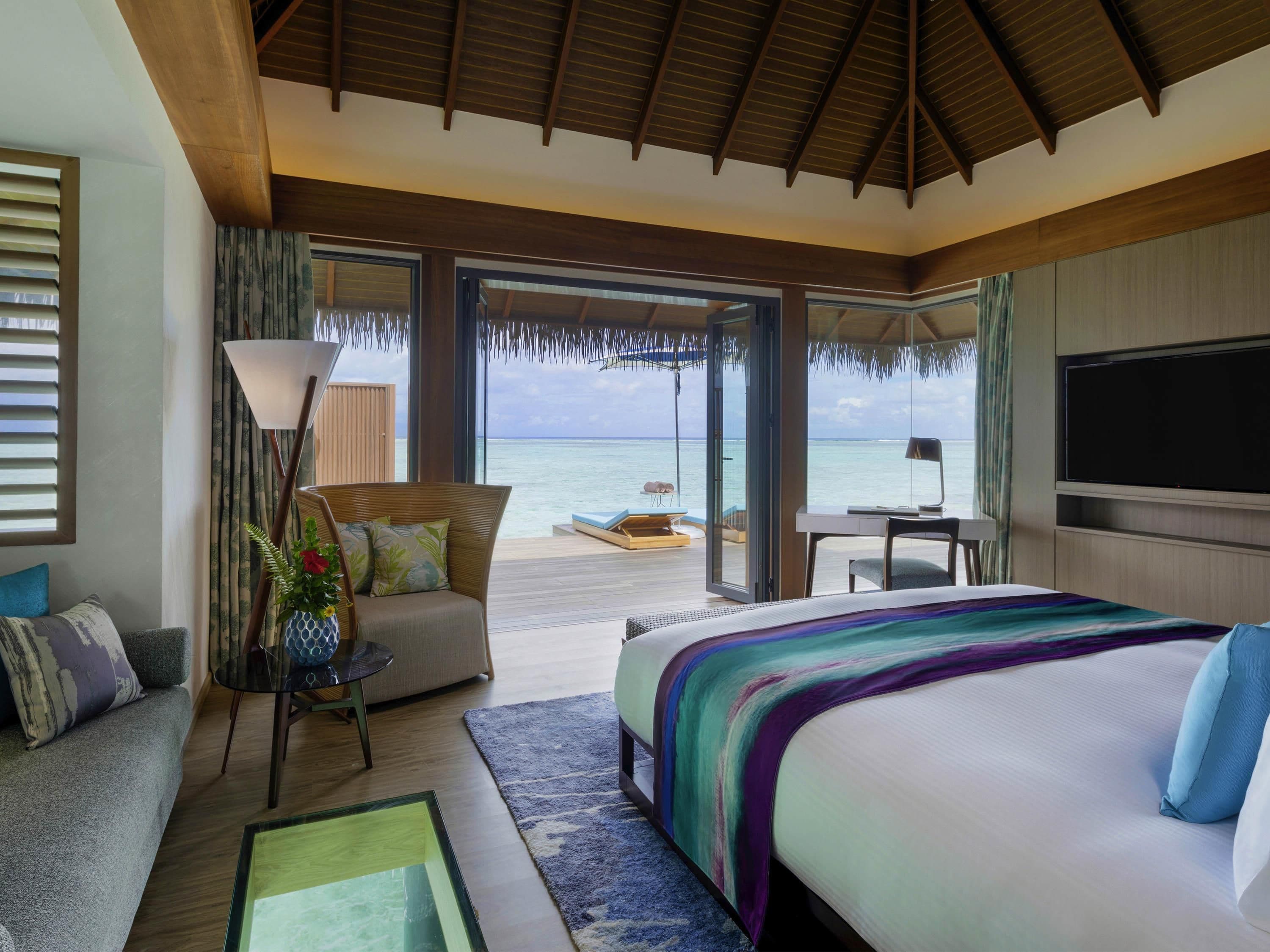 A hotel room with a large bed, a desk, a chair, a sofa, and a view of the ocean.