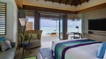A hotel room with a large bed, a desk, a chair, a sofa, and a view of the ocean.