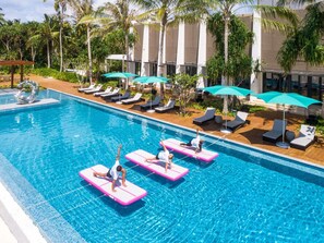 Ein Swimmingpool mit rosa Schwimmbrettern, Liegestühlen und Sonnenschirmen.