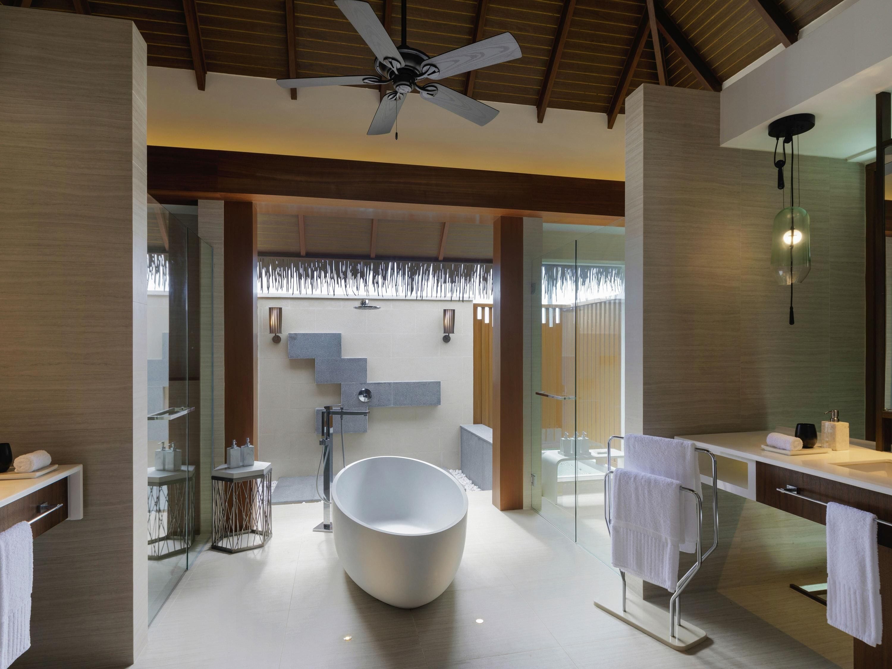 A modern bathroom with a freestanding bathtub, glass shower enclosure, and a ceiling fan.