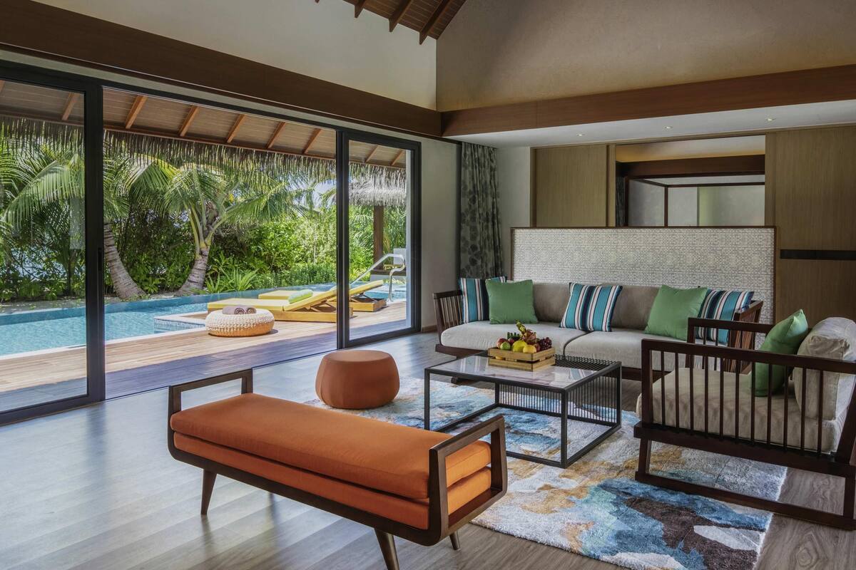 A modern living room with a large glass wall, a pool, and a sofa with cushions.