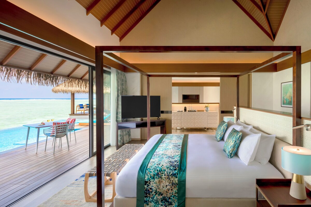 Habitación de hotel moderna con una cama grande, televisión, escritorio y vista al océano.