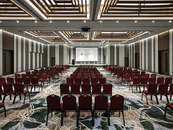 A conference room with rows of red chairs, a large screen, and a podium. - Pullman Phu Quoc Beach Resort (Phu Quoc)