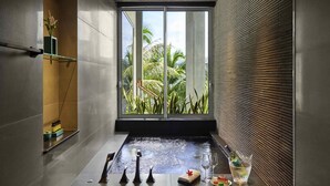 Une salle de spa moderne dotée d’une grande fenêtre, d’un bain à remous et d’un plateau sur lequel se trouvent une bouteille, des verres et un dessert.