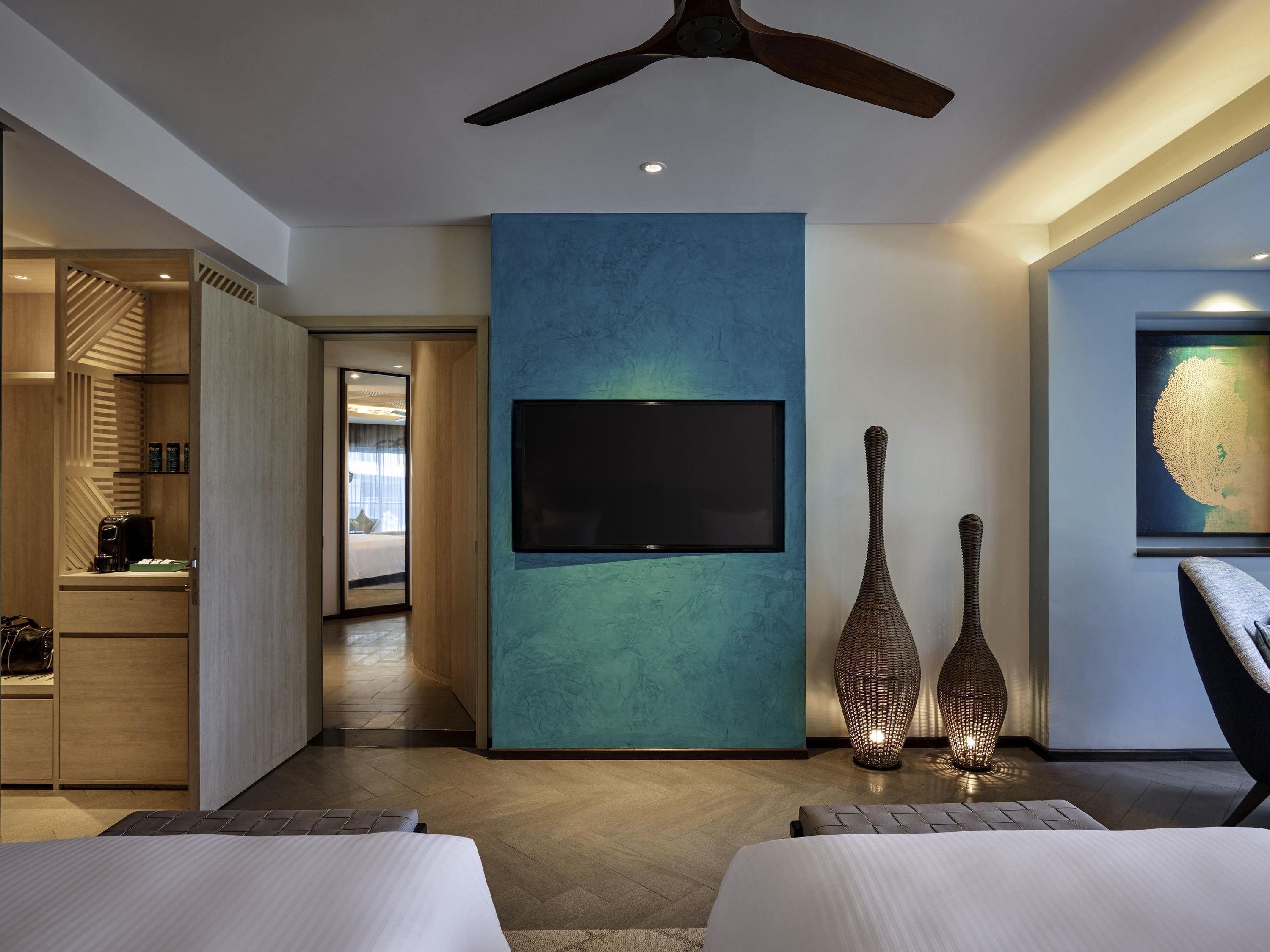 Ein modernes Hotelzimmer mit einem großen Fernseher an einer türkis gefärbten Akzentwand, einem Deckenventilator und einem großen Fenster.