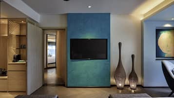 Ein modernes Hotelzimmer mit einem großen Fernseher an einer türkis gefärbten Akzentwand, einem Deckenventilator und einem großen Fenster.