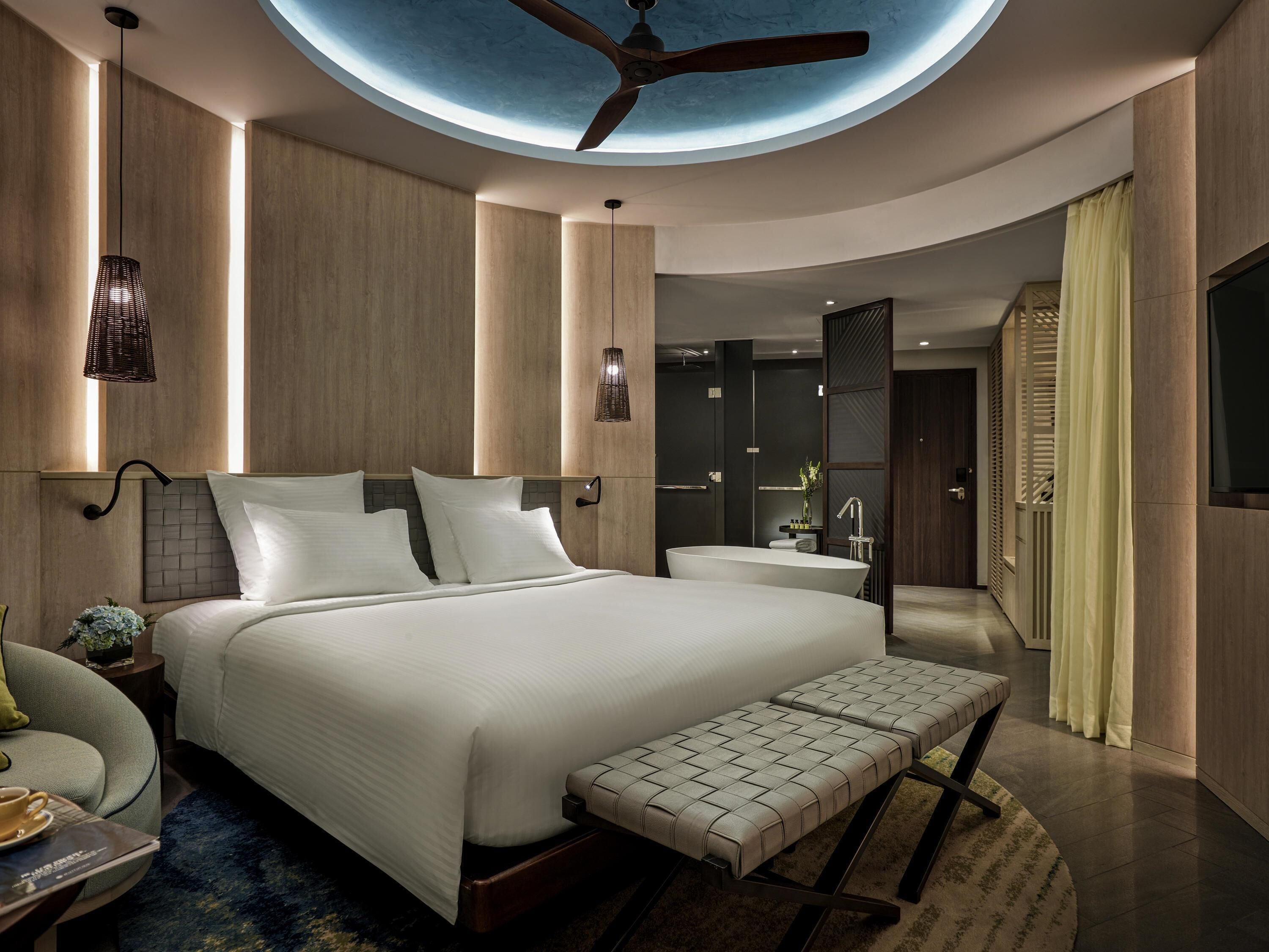 Une chambre moderne avec un grand lit, un banc, un ventilateur de plafond et une lucarne.