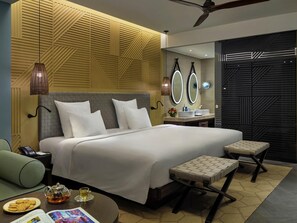 A modern hotel room with a large bed, bedside tables, a vanity with mirrors, and a ceiling fan.