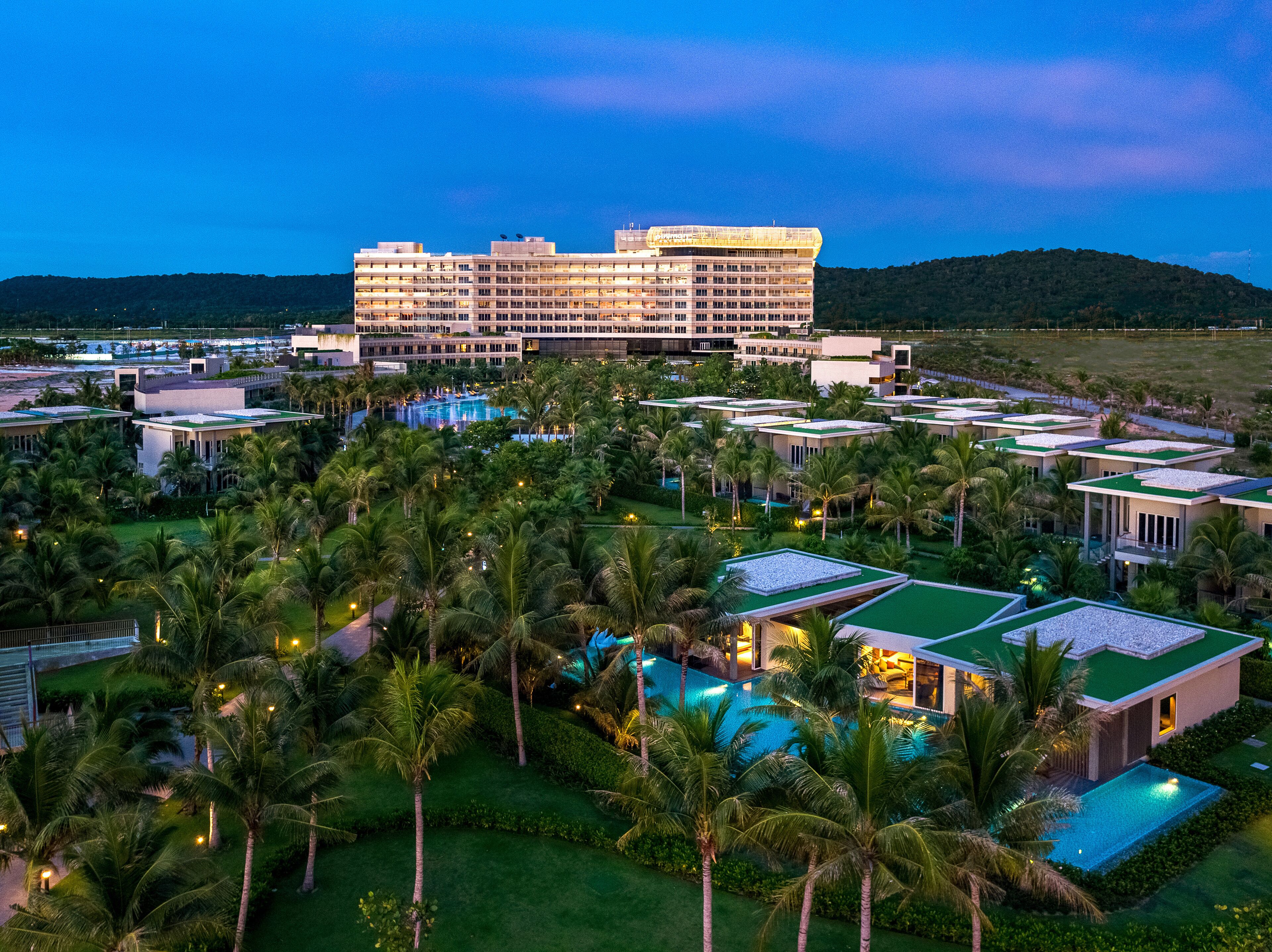 Un hotel grande con varias piscinas rodeado de palmeras y vegetación.