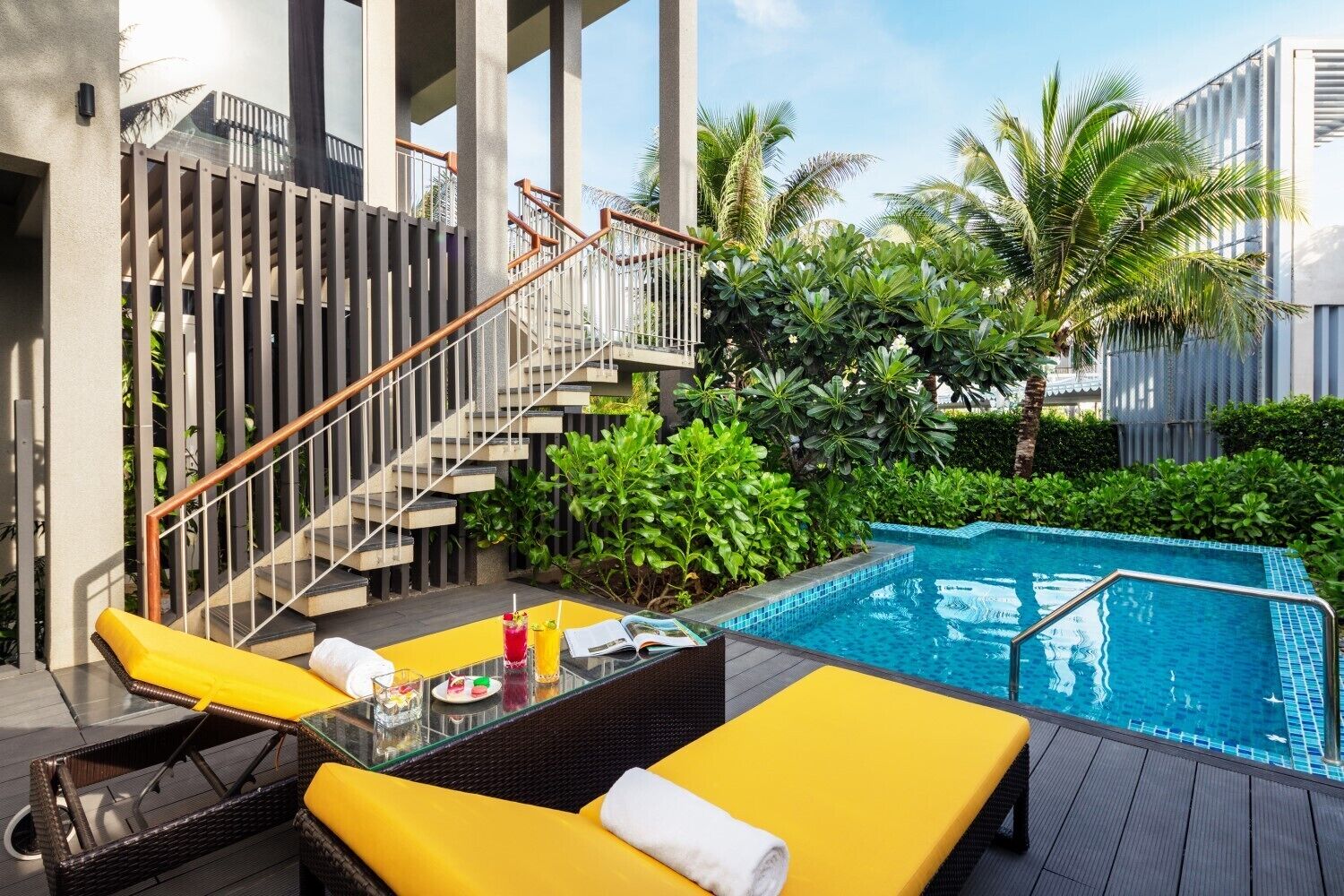 A modern outdoor pool area with a staircase, yellow lounge chairs, and lush greenery.