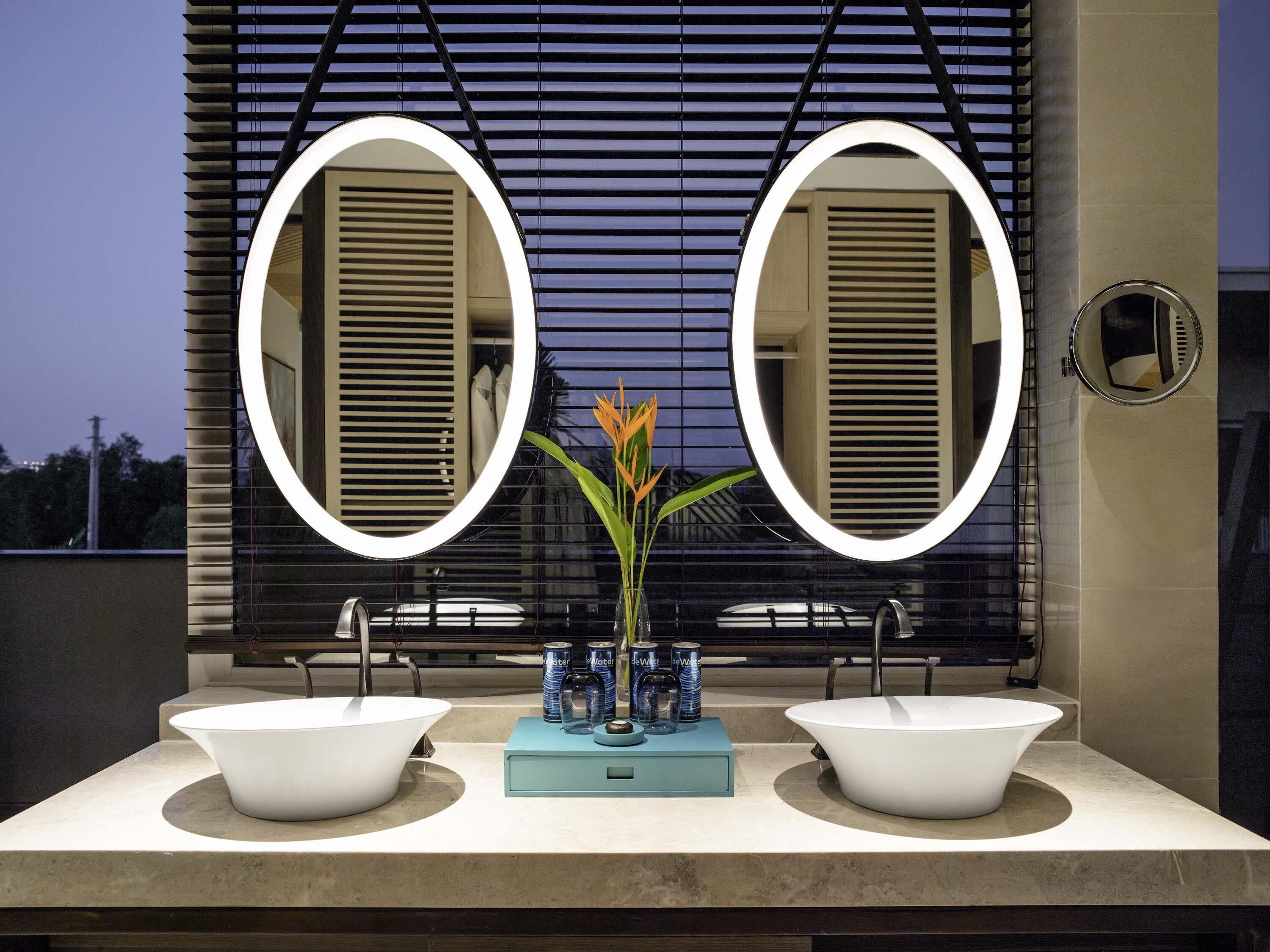 A modern bathroom with two sinks, a mirror, and a vase with flowers.
