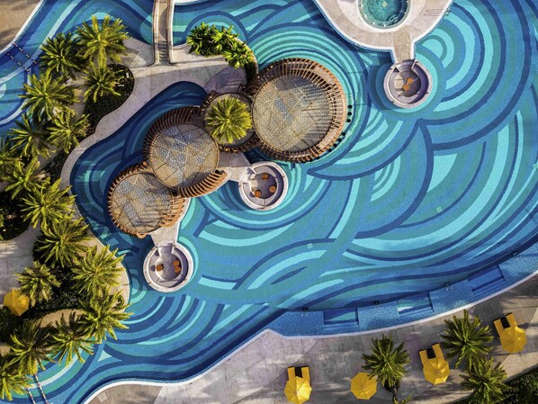 An aerial view of a resort pool area with multiple circular water features, palm trees, and sun loungers. - Pullman Phu Quoc Beach Resort (Phu Quoc)
