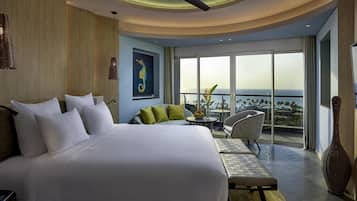 A modern hotel room with a large bed, a seating area, a dining table, and a view of the ocean.