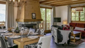 Zona pranzo con tavolo di legno apparecchiato per un pasto, camino e divano rosso sullo sfondo.