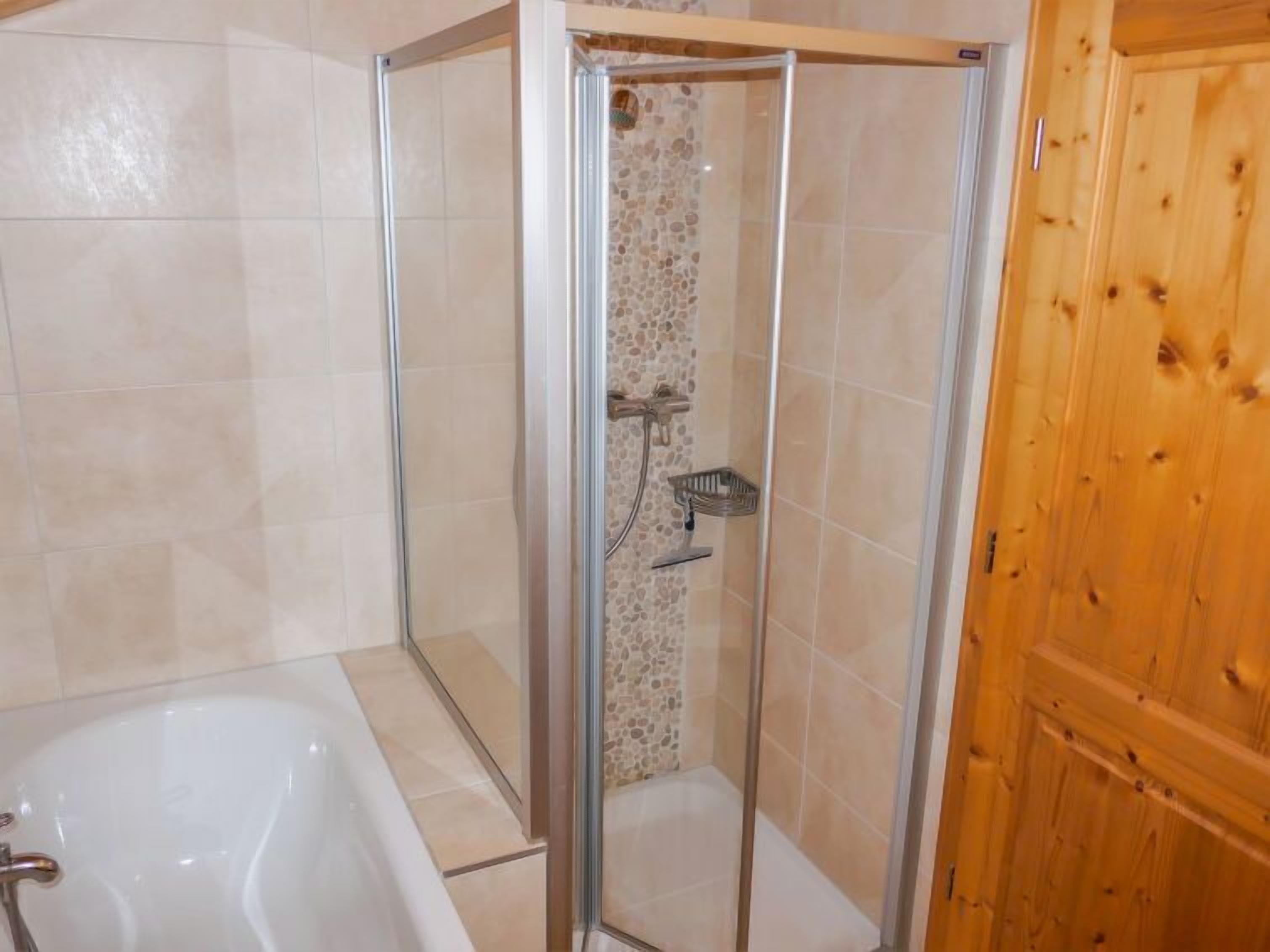 Ein Badezimmer mit einer gläsernen Duschkabine, einer Badewanne und einer Holztür.