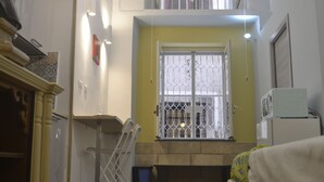 Una habitación con una pared amarilla, una ventana con barrotes de metal, un radiador blanco y una silla blanca.