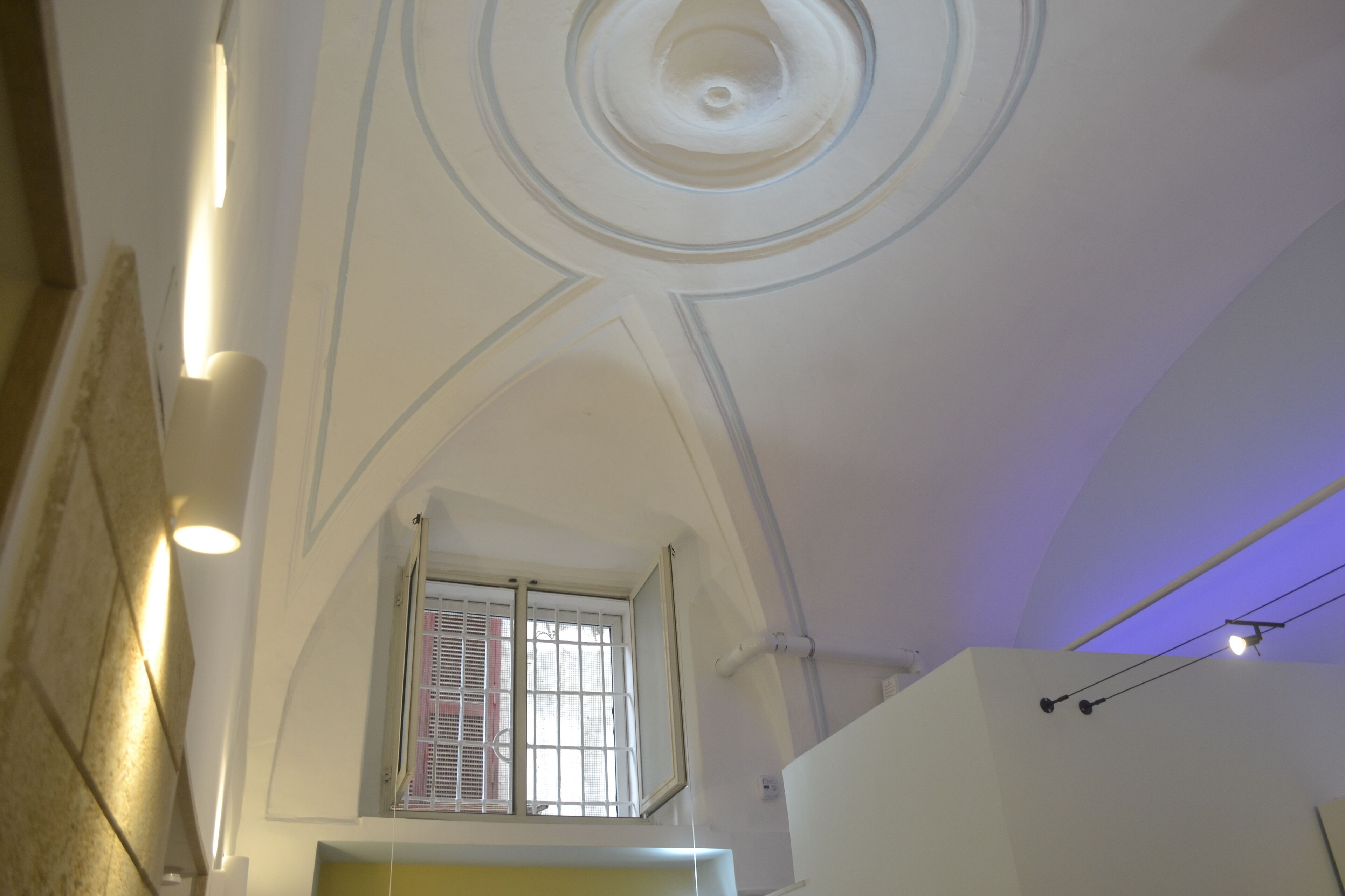 A room with a high ceiling, a window with blinds, and a light fixture.